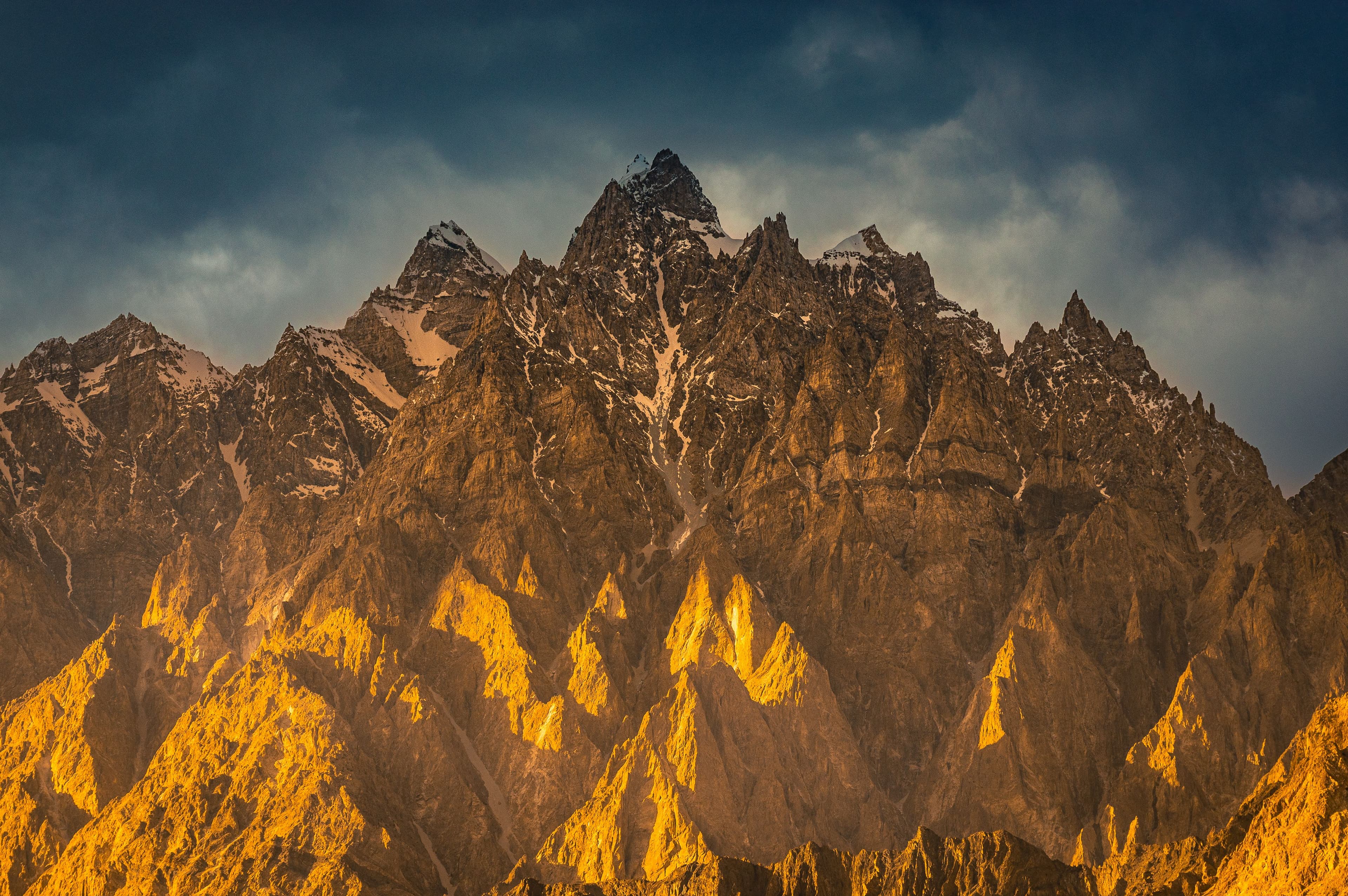 Golden light illuminating rugged mountain peaks under a dramatic sky in the Karakoram range.