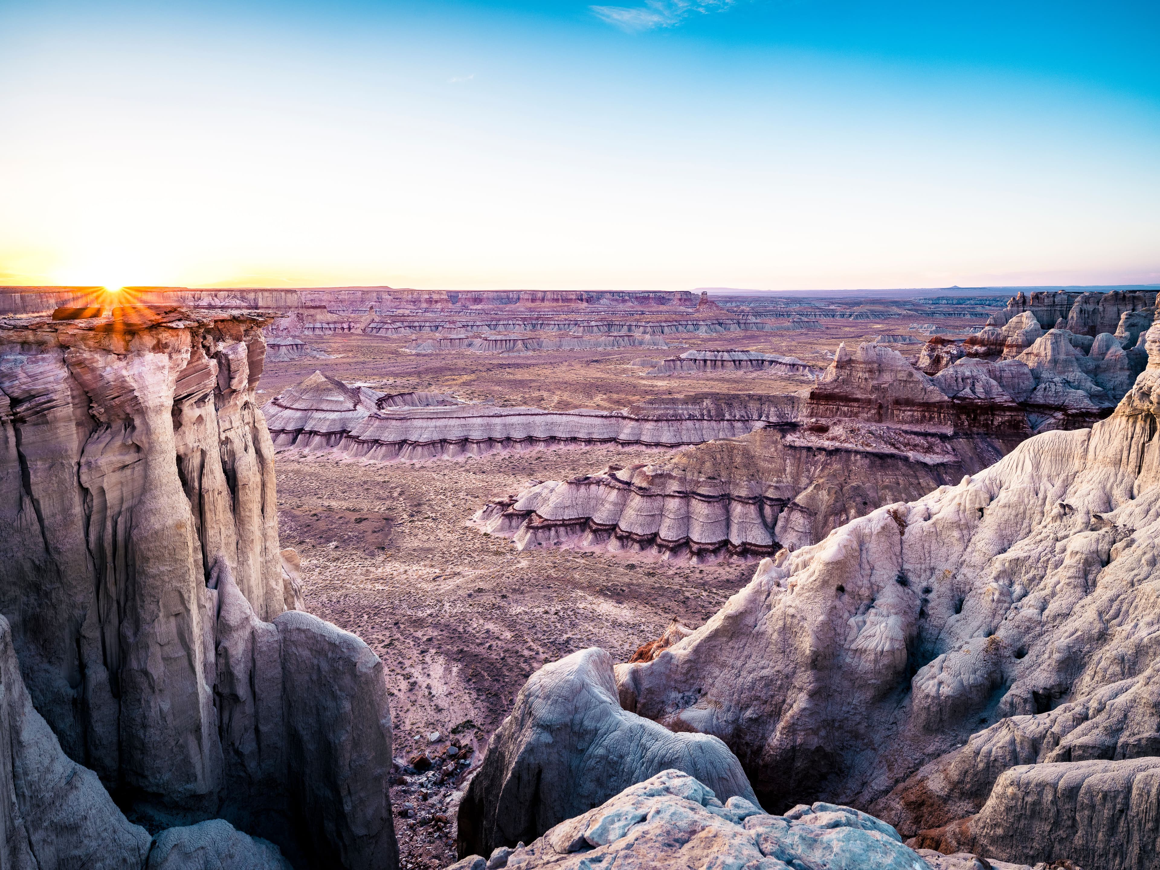 Sunset illuminates grand stone formations and layered cliffs in a vast, silent canyon landscape.